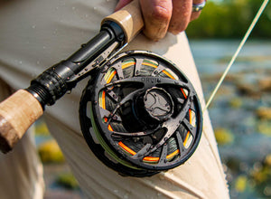 Close up of a wet Orvis Mirage fly reel held against an anglers hip