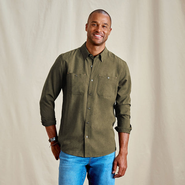 Man wearing an olive green shirt and blue jeans against a beige background