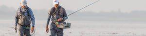 two men wearing full fly fishing gear walking by the sea
