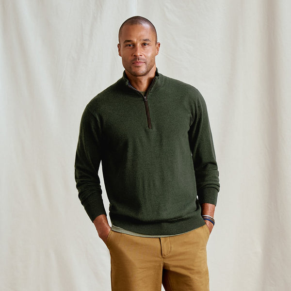 Man wearing a green sweater with a quarter zip and brown pants against a plain background