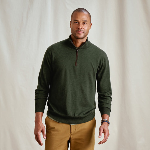 Man wearing a green sweater and brown pants against a plain background