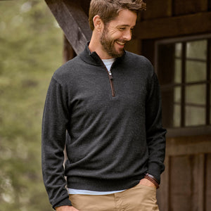 Man wearing a dark gray pullover with a wooden building in the background