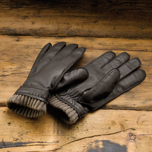 Pair of dark brown leather gloves with knitted cuffs on a wooden surface