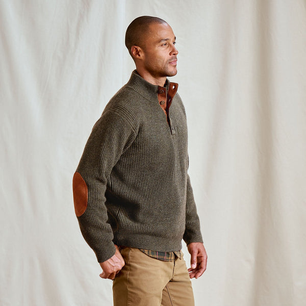 Man wearing a brown sweater with elbow patches against a plain background