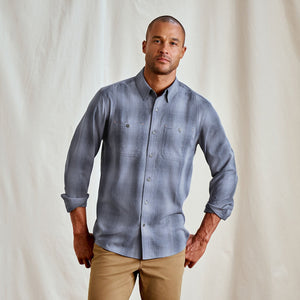 Man wearing a blue checkered shirt and beige pants against a plain background