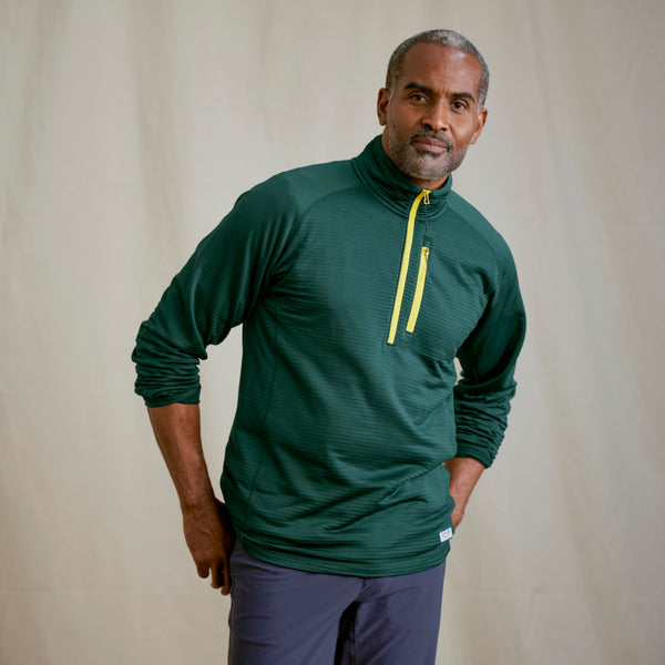 Man facing camera modelling dark green sweater and blue pants