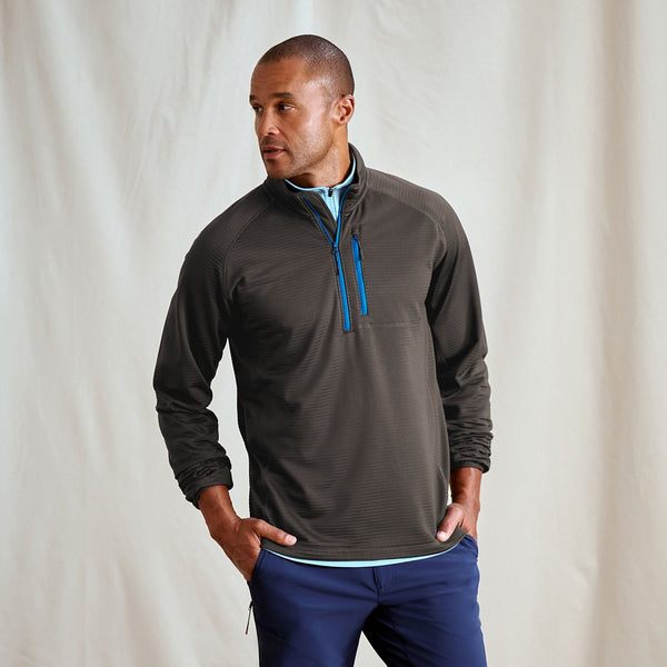 Man wearing a brown pullover with a blue zipper against a plain background