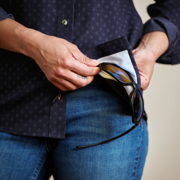 Person holding sunglasses in a dark blue case against a neutral background