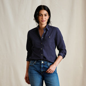 Woman wearing a dark blue patterned shirt and jeans against a beige background
