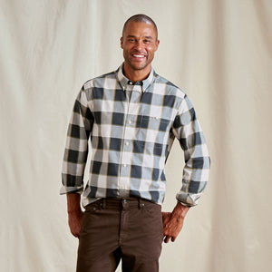 Man wearing a plaid shirt and brown pants against a plain background