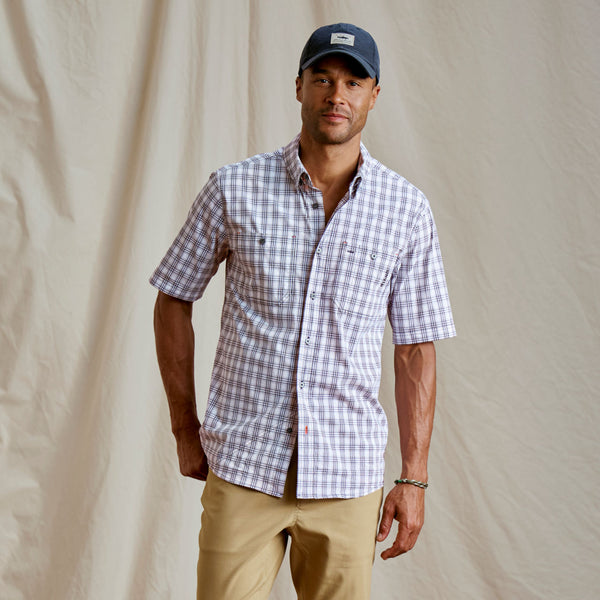 Man facing camera modeling blue cap, short sleeved shirt and beige pants