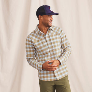 Man smiling wearing beige and white checkered shirt and blue fishing cap