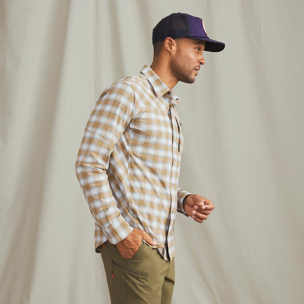 Man wearing blue cap, beige and white checkered shirt and military green pants in front of beige background