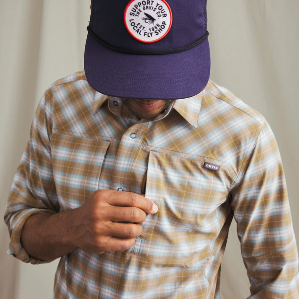 Man wearing fly cap and white and beige checkered shirt in front of beige background