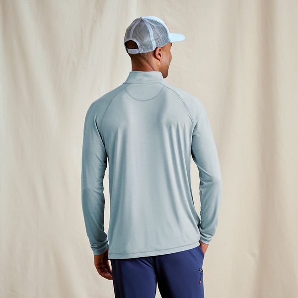 Man wearing a light blue long-sleeve shirt and dark blue pants against a beige background