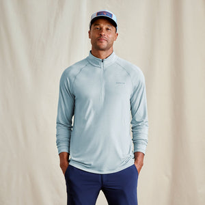 Man wearing a light blue athletic jacket and navy pants against a beige background