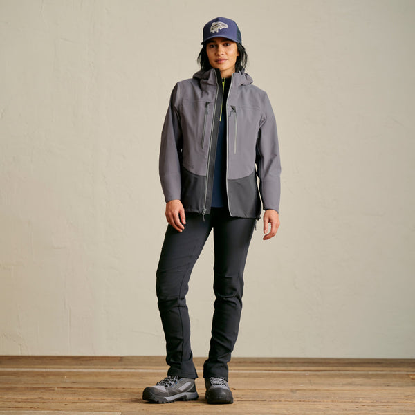 woman wearing dark grey pants, wading boots and jacket and dark blue cap