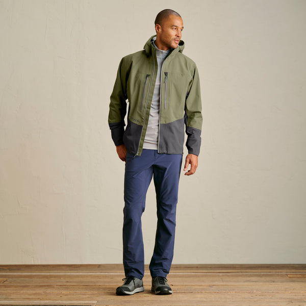 man wearing green waterproof jacket and blue pants and wading boots