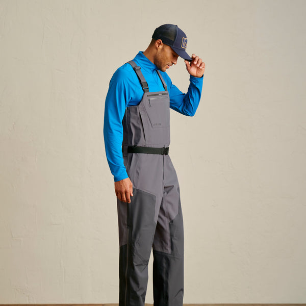 man wearing Orvis waders, blue sweater and dark blue fishing cap