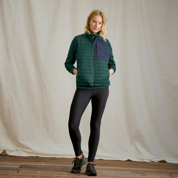 woman facing camera wearing dark green fishing vest and black leggings