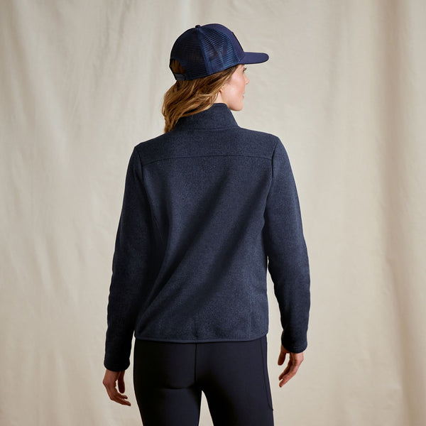 Person wearing a navy jacket and cap on a beige background