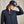 Load image into Gallery viewer, Woman wearing a navy blue jacket and cap with a visible brand logo on a beige background
