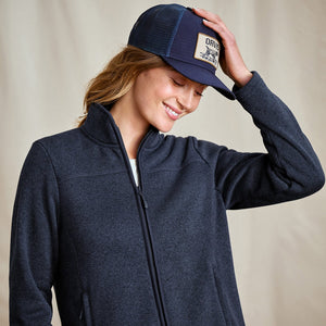 Woman wearing a navy blue jacket and cap with a visible brand logo on a beige background
