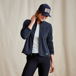 Person wearing a navy jacket, white shirt, and black pants with a matching cap on a beige background