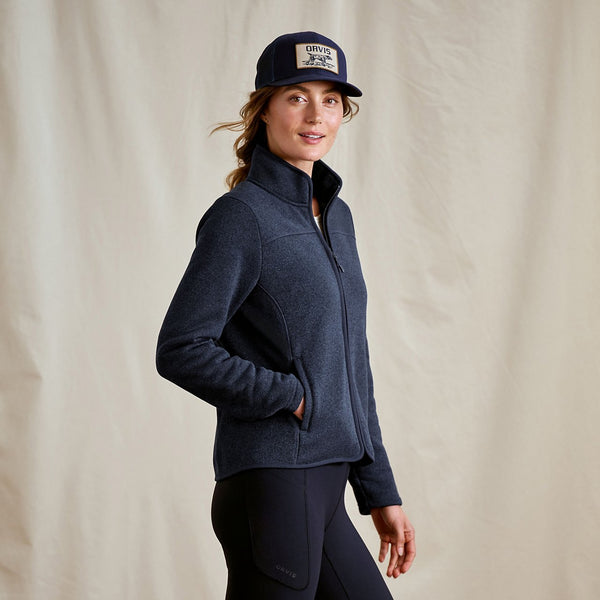 Woman wearing a navy jacket and cap against a beige background