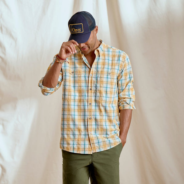 man in dark green shorts, orange checkered shirt and Orvis cap