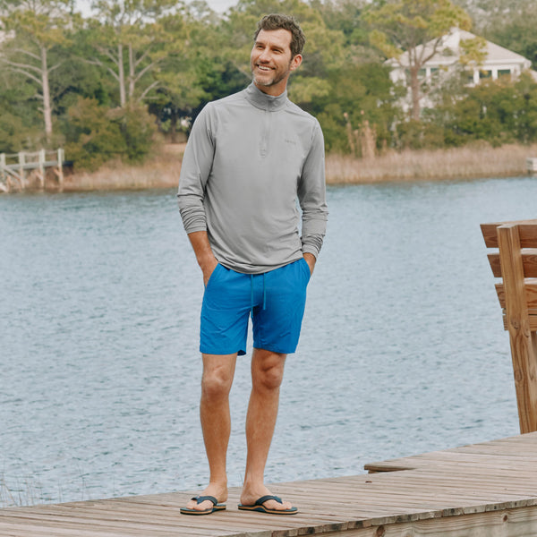 man by the water wearing blue shorts and grey turtleneck sweater