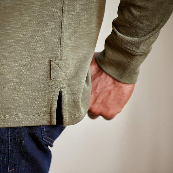 Person wearing a green long-sleeve shirt with a pocket detail on a blurred background
