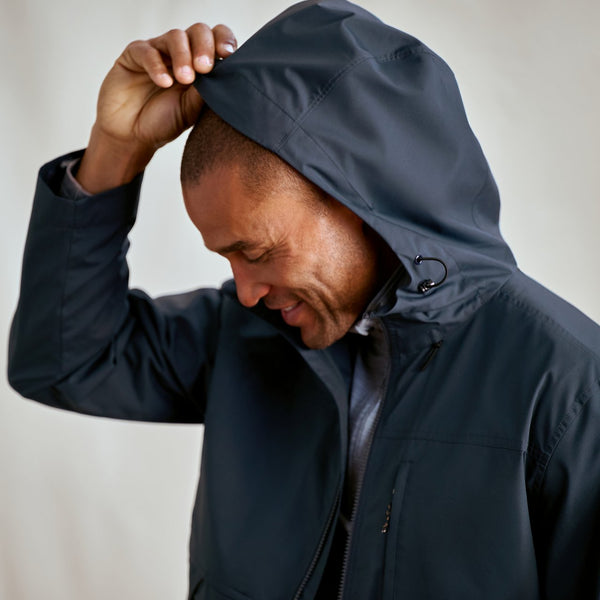 Man wearing a dark jacket with a hood against a plain background