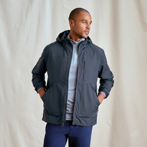Man wearing a dark grey jacket with a hood against a plain background