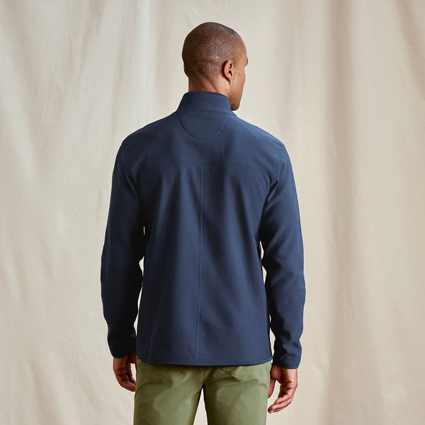 Man wearing a navy jacket and green pants against a beige background