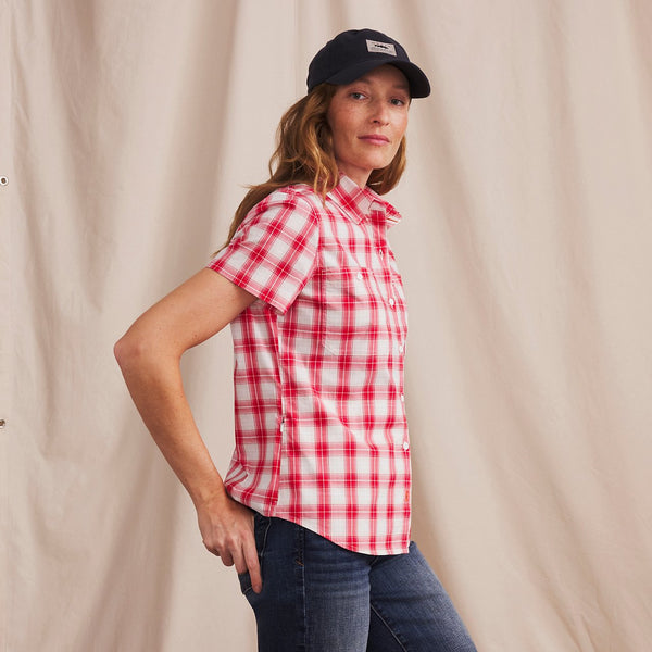 woman looking into the camera wearing jeans, red and white checkered shirt and black cap