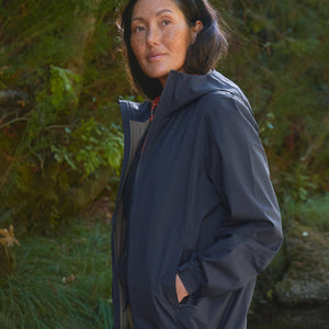 Person wearing a dark blue raincoat standing outdoors with greenery in the background
