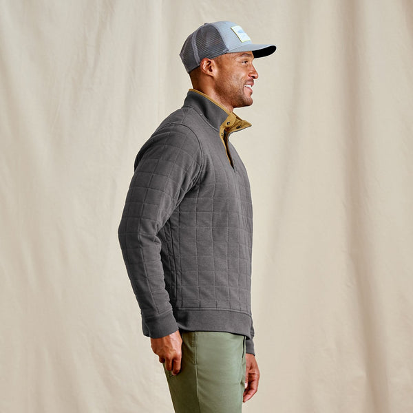 Man wearing a grey quilted jacket and cap against a beige background