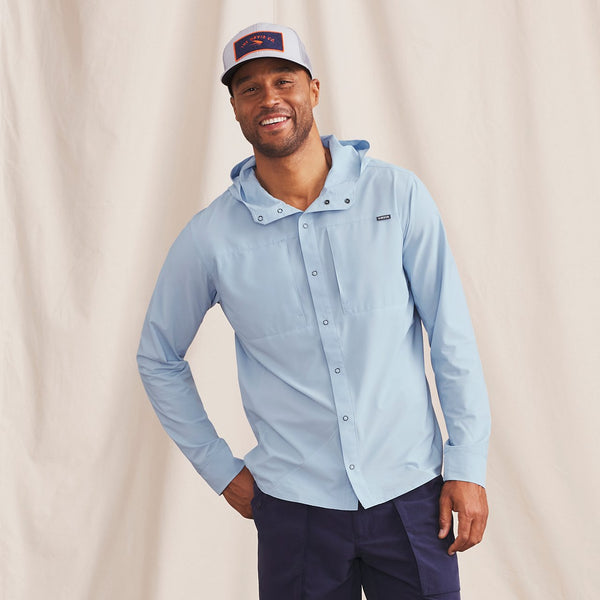 man smiling to camera wearing light blue waterproof jacket and cap with fish logo