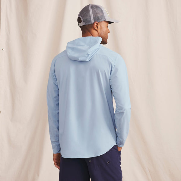 man with his back to the camera wearing cap, light blue hoodie and dark blue pants in front of beige background
