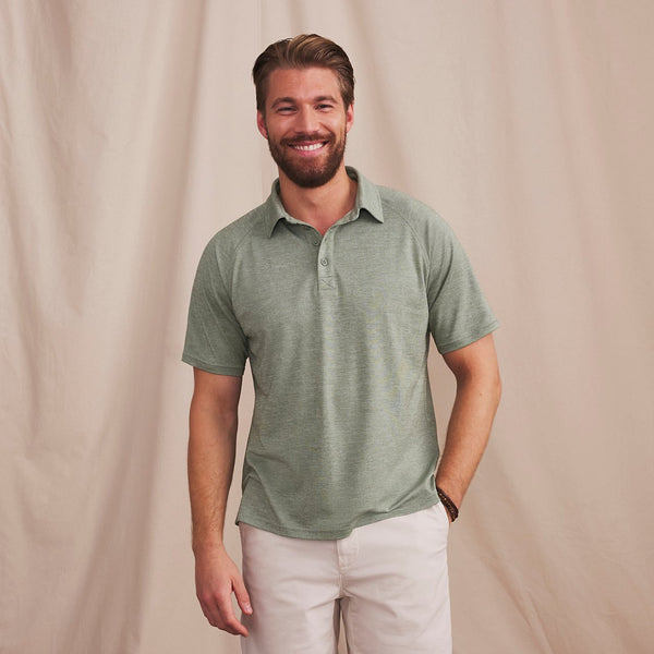 man with brown hair and beard smiling to the camera wearing green  poloshirt and white trousers