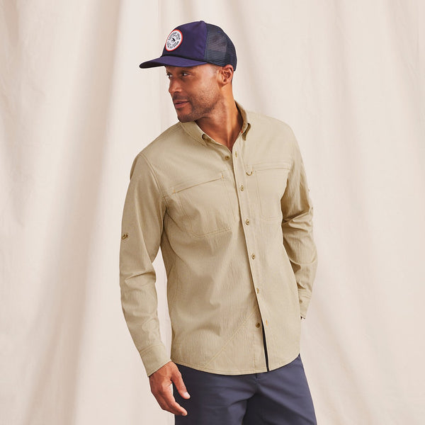 man wearing beige shirt, blue pants and caps in front of beige background