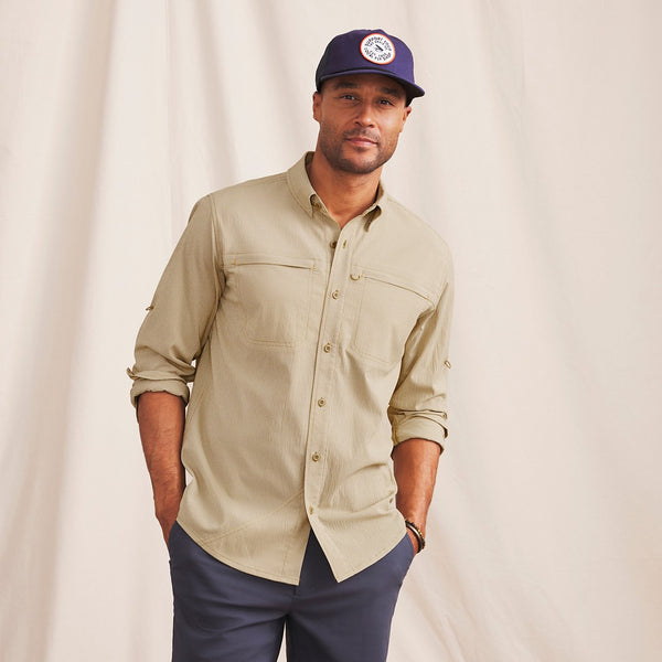 man facing camera wearing blue cap, beige shirt and blue pants