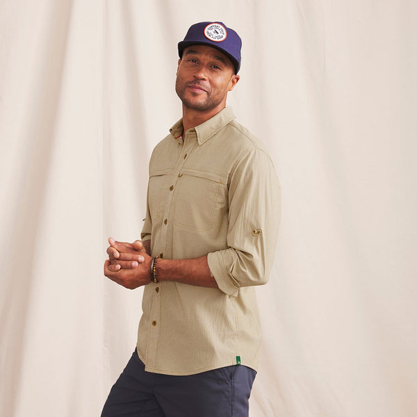 man looking into the camera wearing blue cap, beige shirt and blue pants