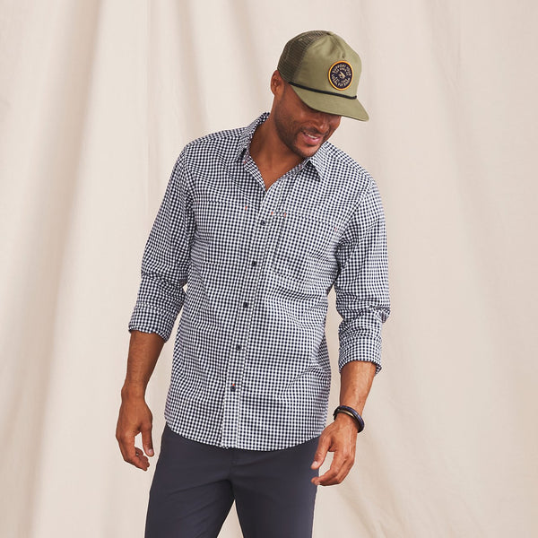 man in front of beige background wearing green cap, checked shirt and blue pants