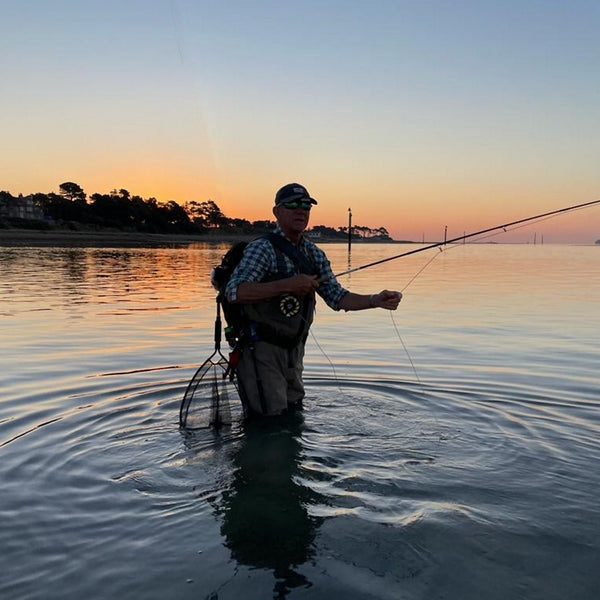 man wading in river at sunset