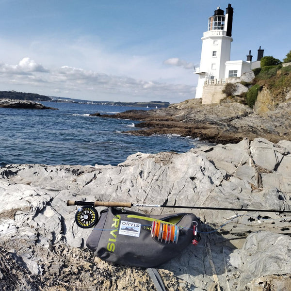 Orvis fishing pack and fly rod laying on stones