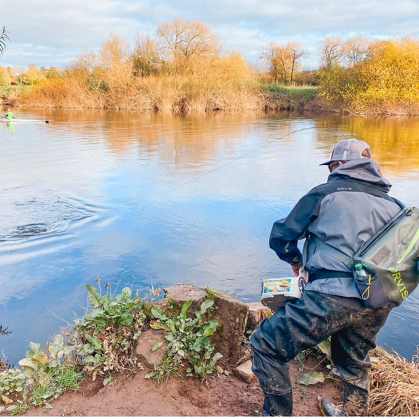 man on riverbank hauling in fish