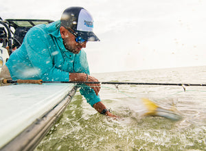 Man fishing from a boat in a blue jacket, catches blurry yellow fish in the water