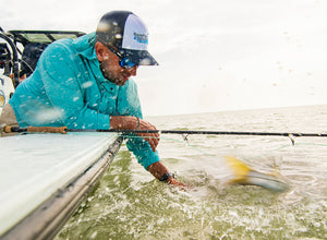Man fishing from a boat in a blue jacket, catches blurry yellow fish in the water